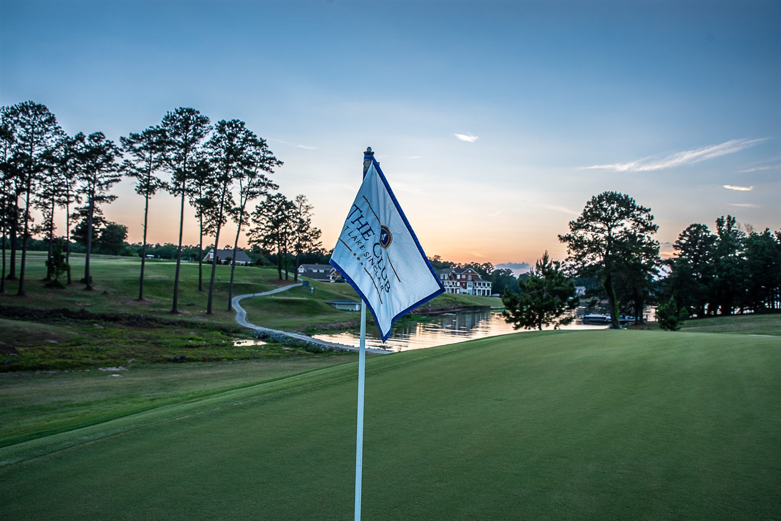 Sunset over a green at The Club at Lake Sinclair, the club's pin flag in the foreground and Lake Sinclair beyond